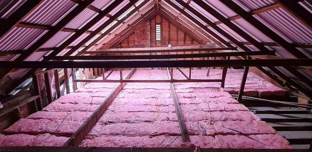 Pink ceiling insulation batts fitted between timber joists in a roof space