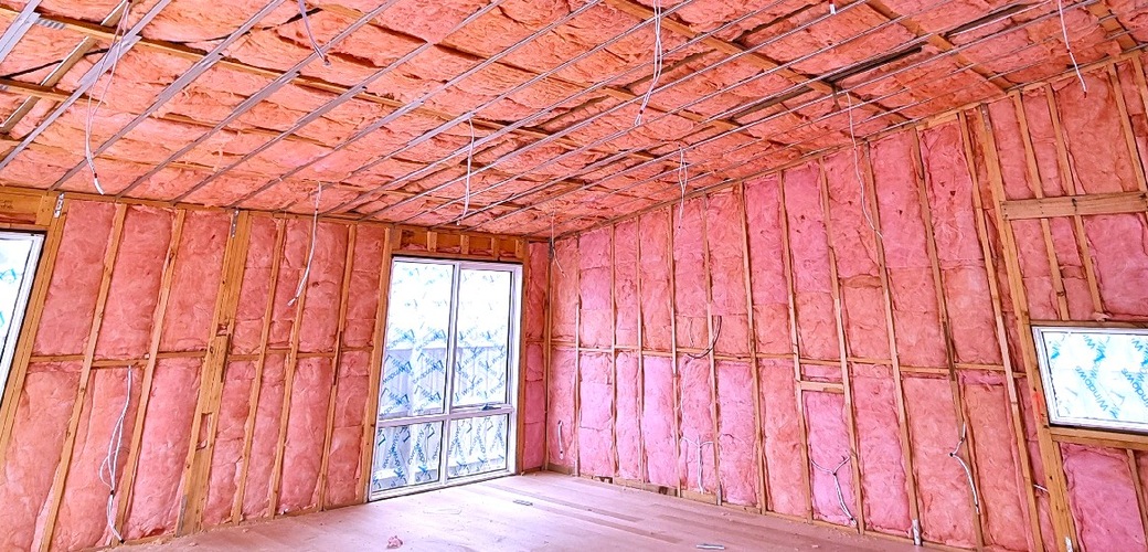 Pink insulation fitted between wall studs and ceiling framing in a new build
